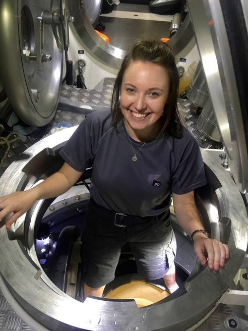 Young female wearing a jfd tshirt popping up through a circular door in the floor of a submarine