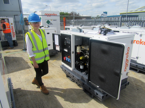 young female in high vis waistcoat stood next to an aggreko piece of equipment